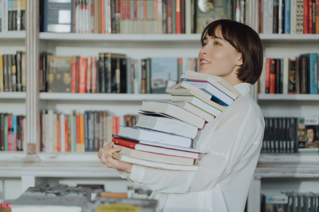 Una mujer cargando varios libros que tienen términos financieros.